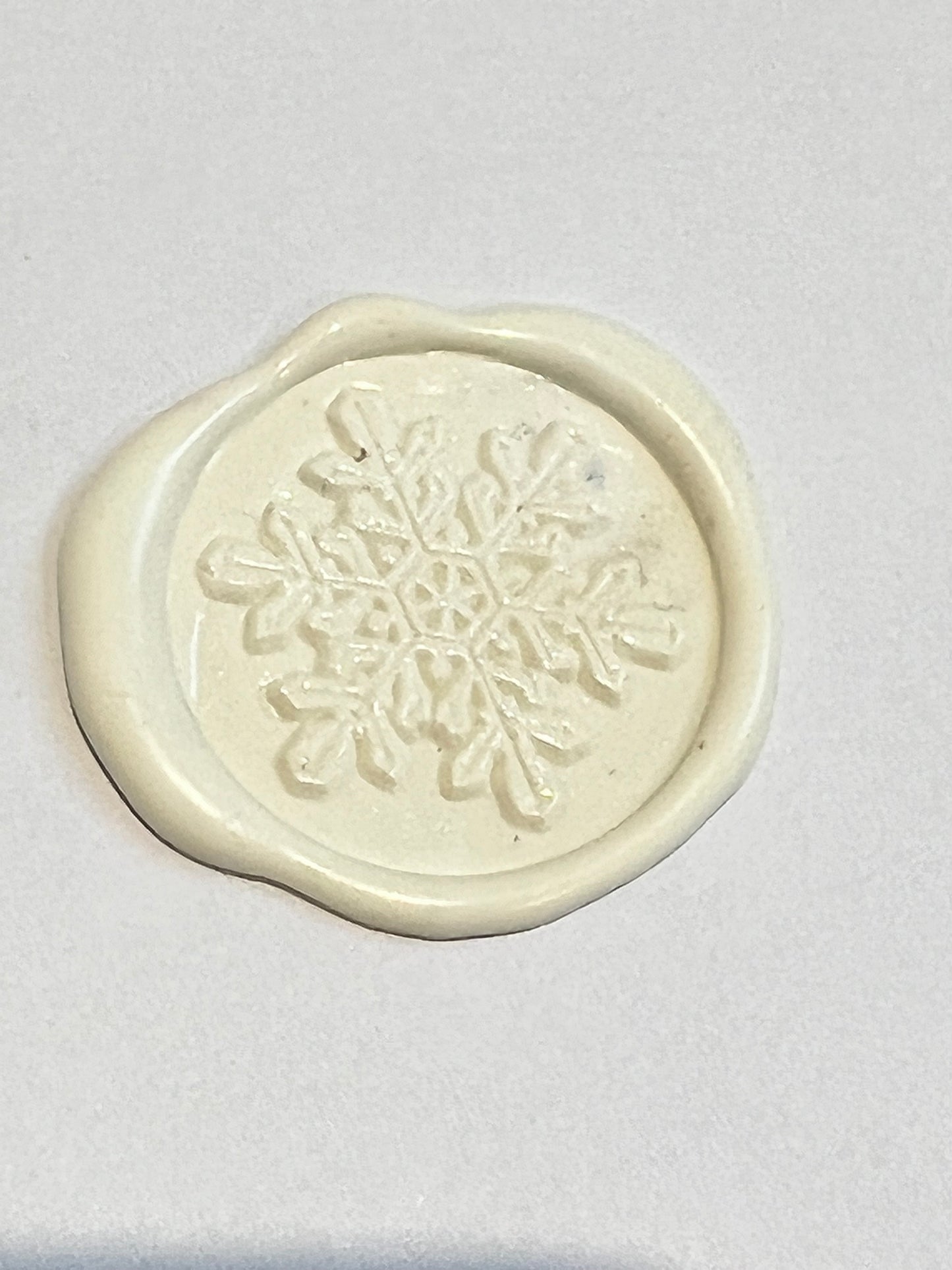 white wax seal snowflake design on white background.