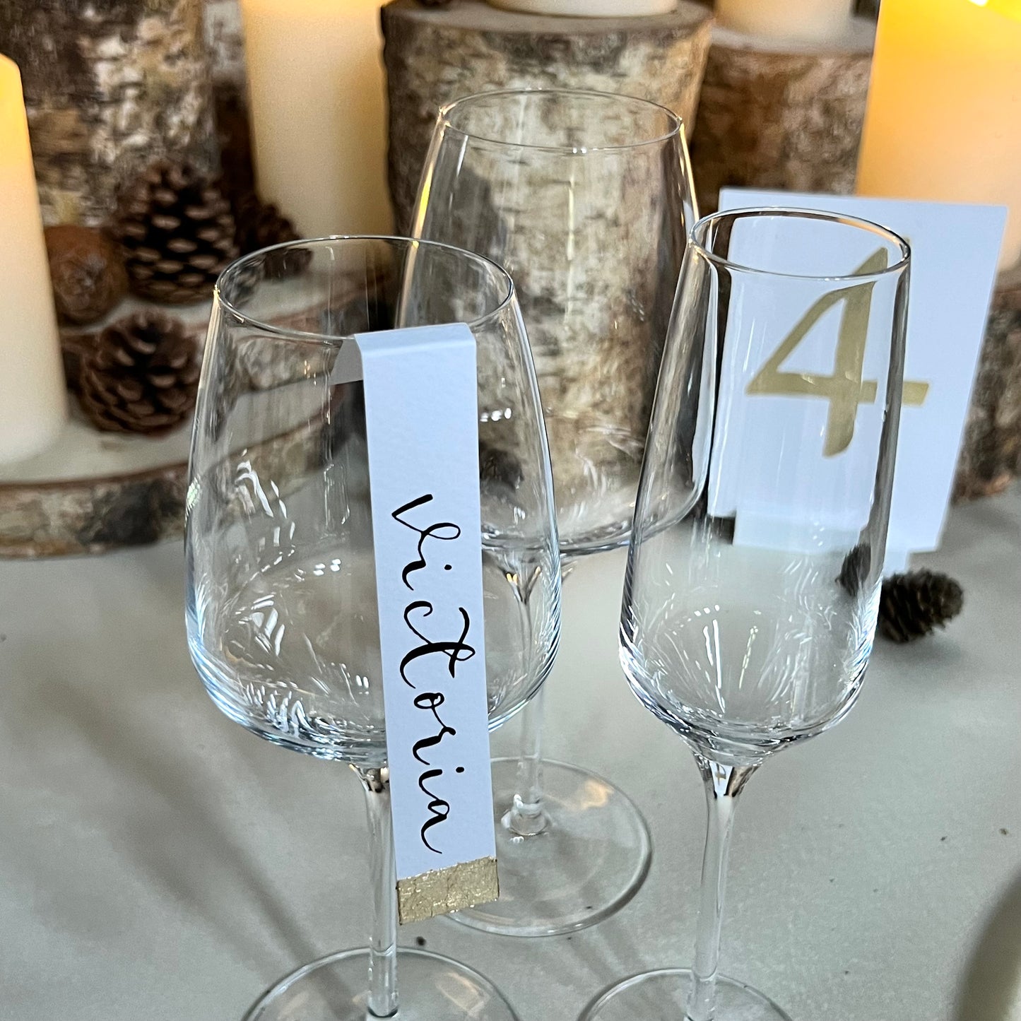 table set up with wine glasses, guest name tag on side of one wine glass. Tag has gold leaf at bottom and black ink calligraphy name